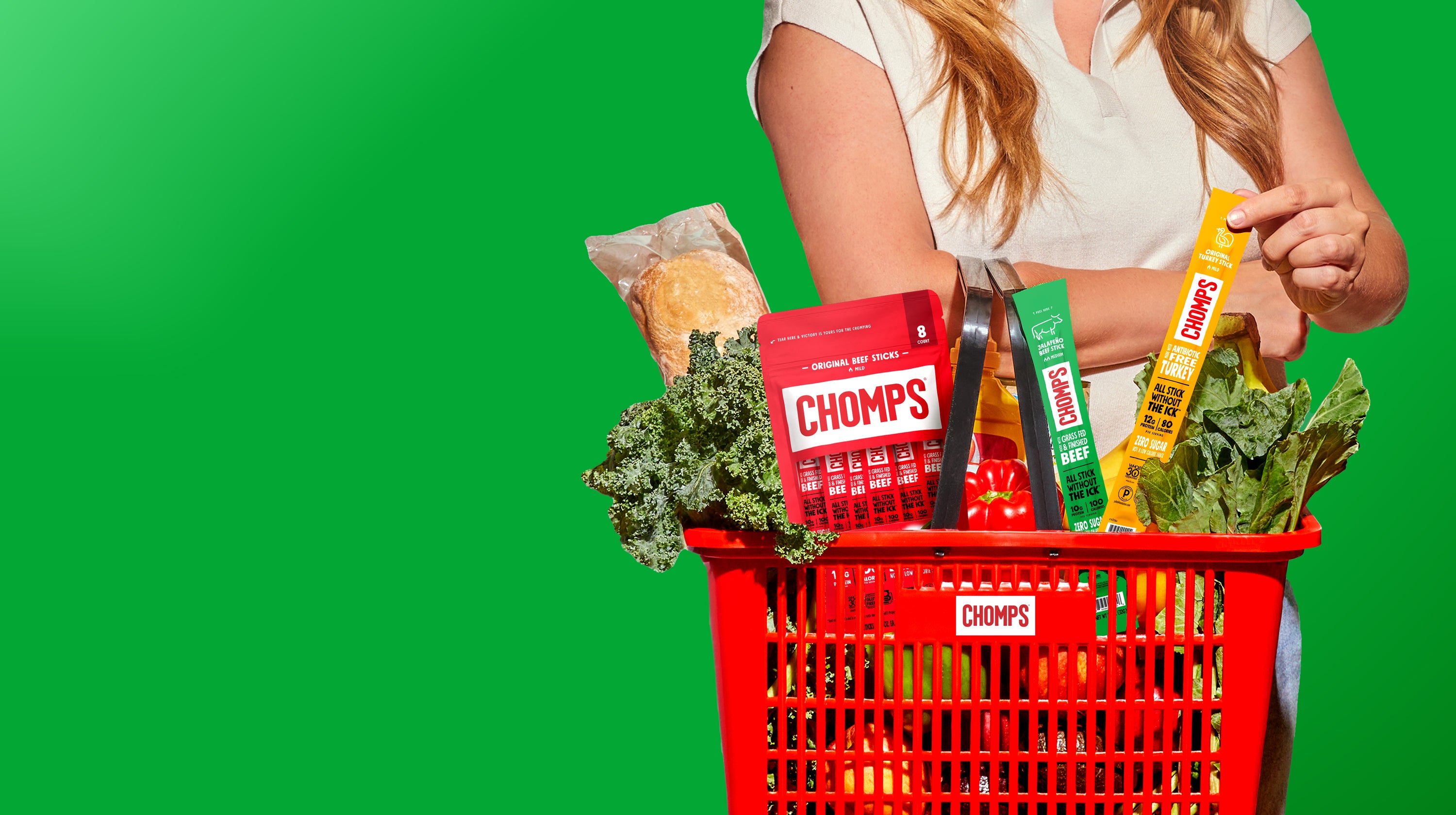 A woman holding a shopping basket with fruits, vegetables, bread, and an assortment of Chomps