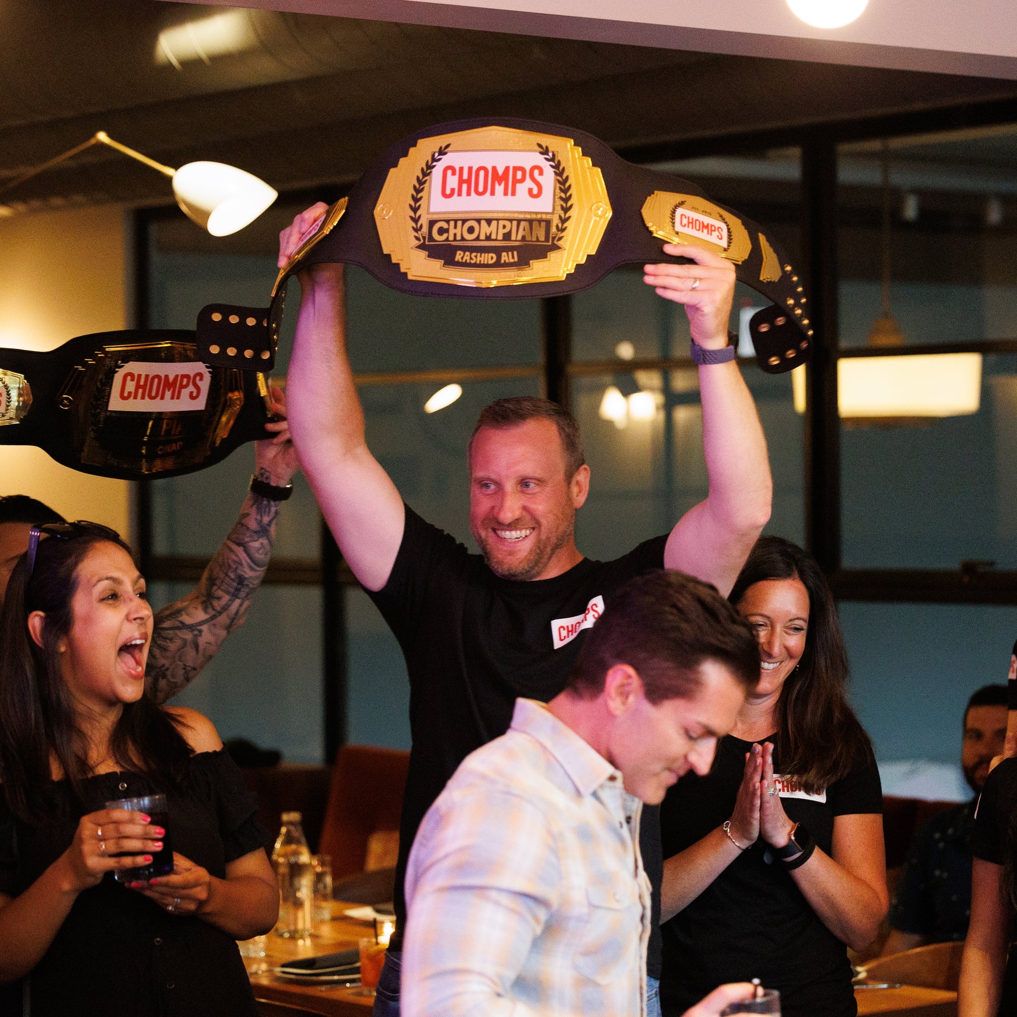 Chomps Employees celebrating by holding Chomps themed wrestling belts over their heads while at the company party